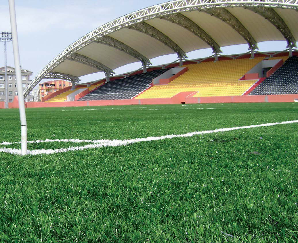 Terrain de football en gazon synthétique, tribune couverte, vue au niveau du sol.