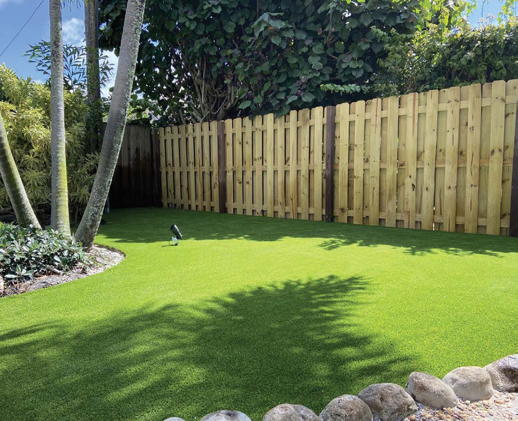 Jardin résidentiel en gazon synthétique, clôture bois et végétation.