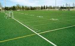 Terrain de football en gazon synthétique haute densité, lignes de jeu blanches, terrain vide.