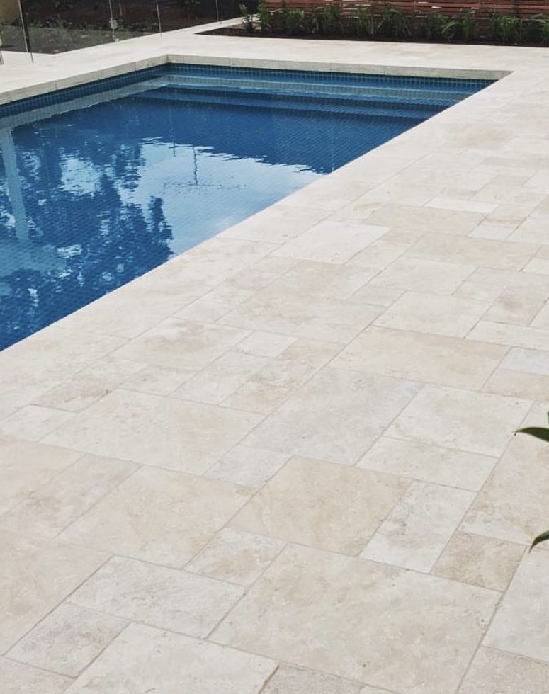 Plage de piscine en travertin Ivory, teinte crème claire, pose French Pattern.